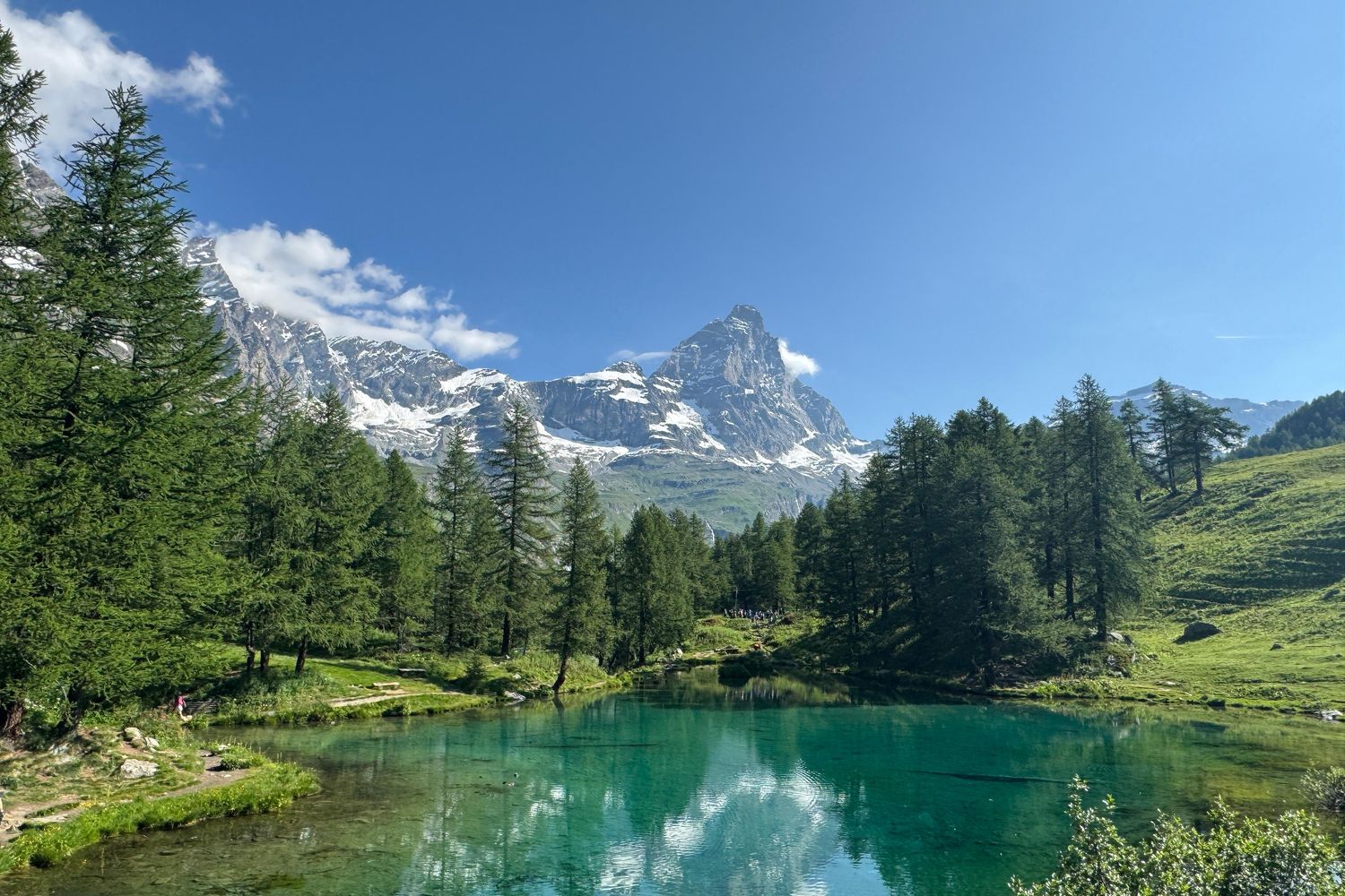 Breathtaking panorama of the Matterhorn rising above pine forests and a turquoise lake with perfect reflections.