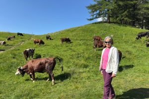 Smiling woman standing in a green alpine pasture among grazing cows in the Swiss or Italian Alps.